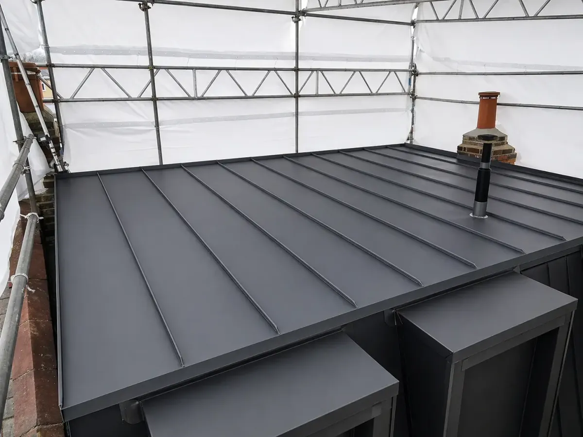 Dark zinc standing seam roof under construction with vent penetrations